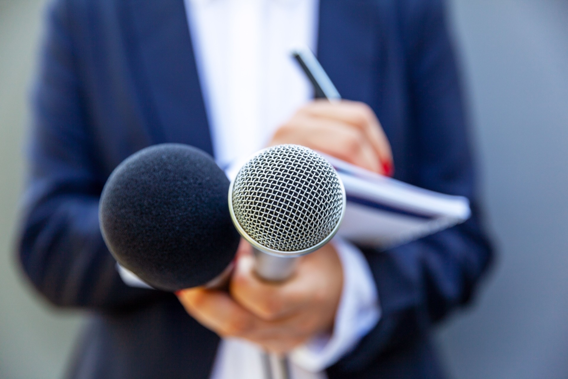 Female journalist at news conference or media event, writing notes, holding microphone